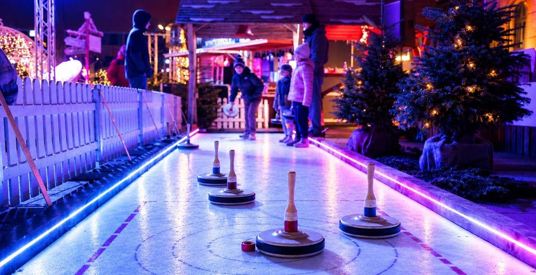 Gäste beim Eisstockschießen zwischen Tannenbäumen